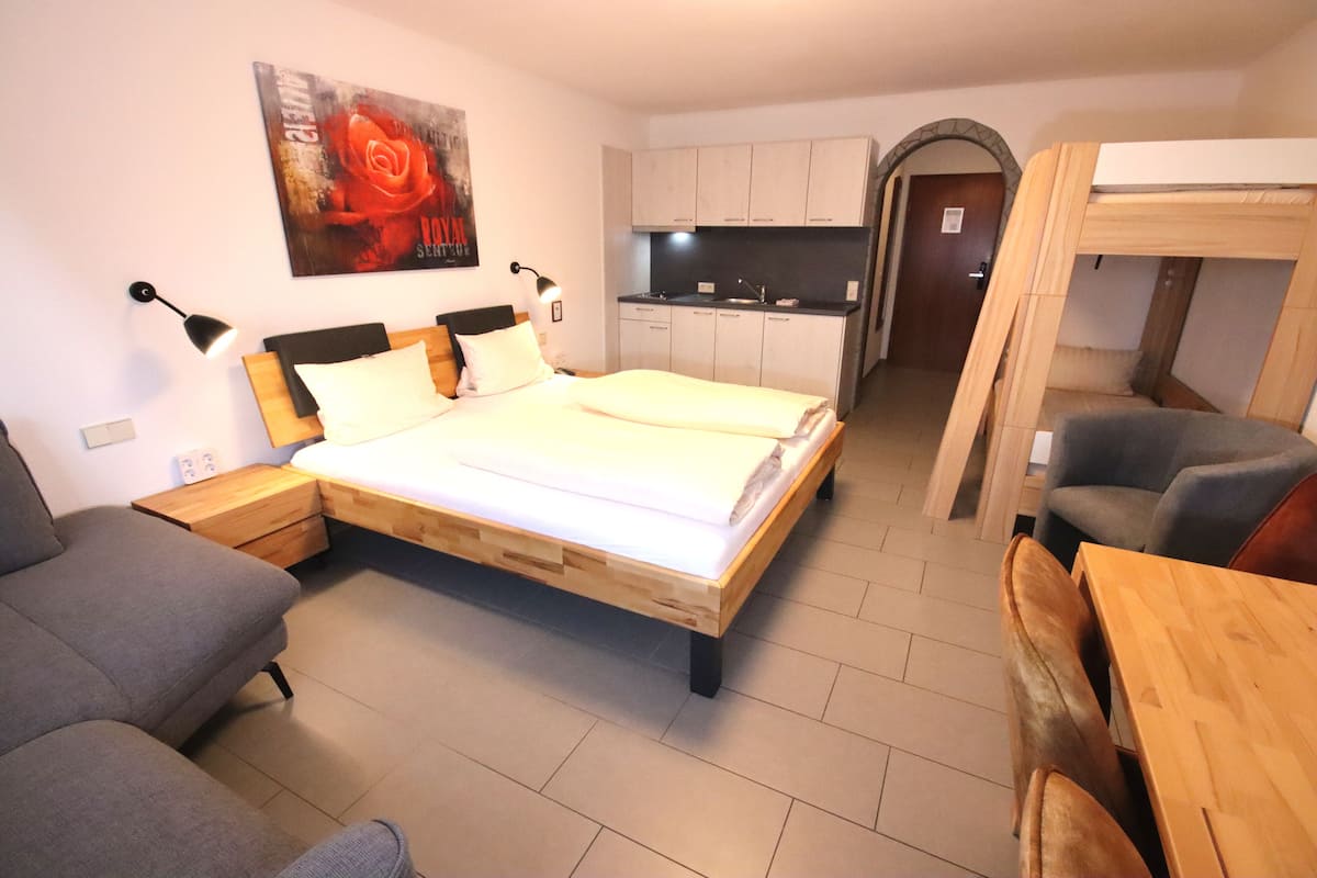 Un dormitorio con cama, sofá, una mesa de madera y una kitchenette al fondo.