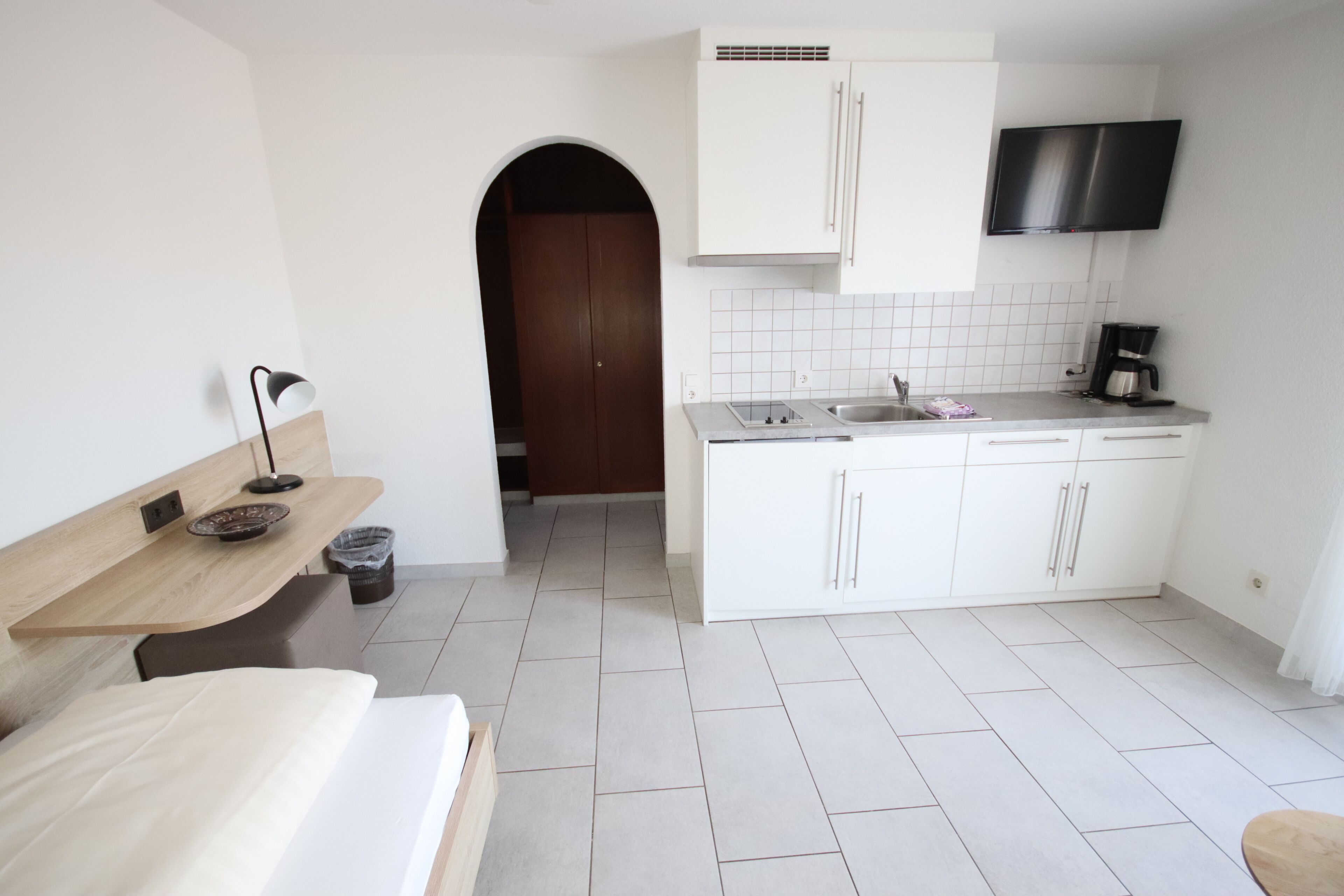 Habitación de hotel compacta con kitchenette, cama, escritorio y televisor sobre la encimera.