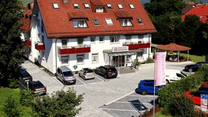 A hotel with a red-tiled roof, multiple windows, and a parking lot with several cars. - Appartements Biedermeier (Bad Krozingen)