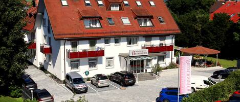 A hotel with a red-tiled roof, multiple windows, and a parking lot with several cars.