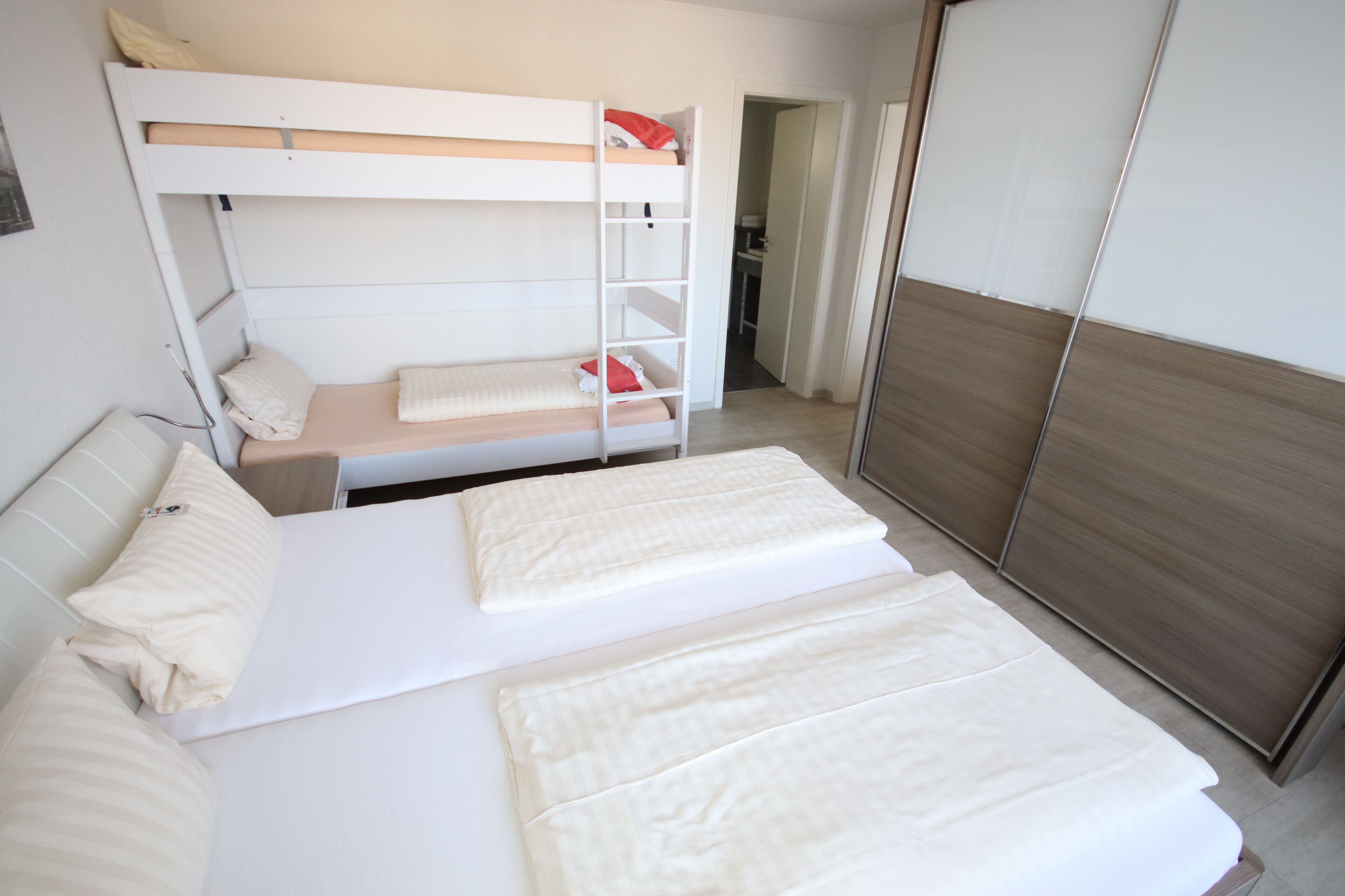 A bedroom with two beds, a bunk bed, and a wardrobe.