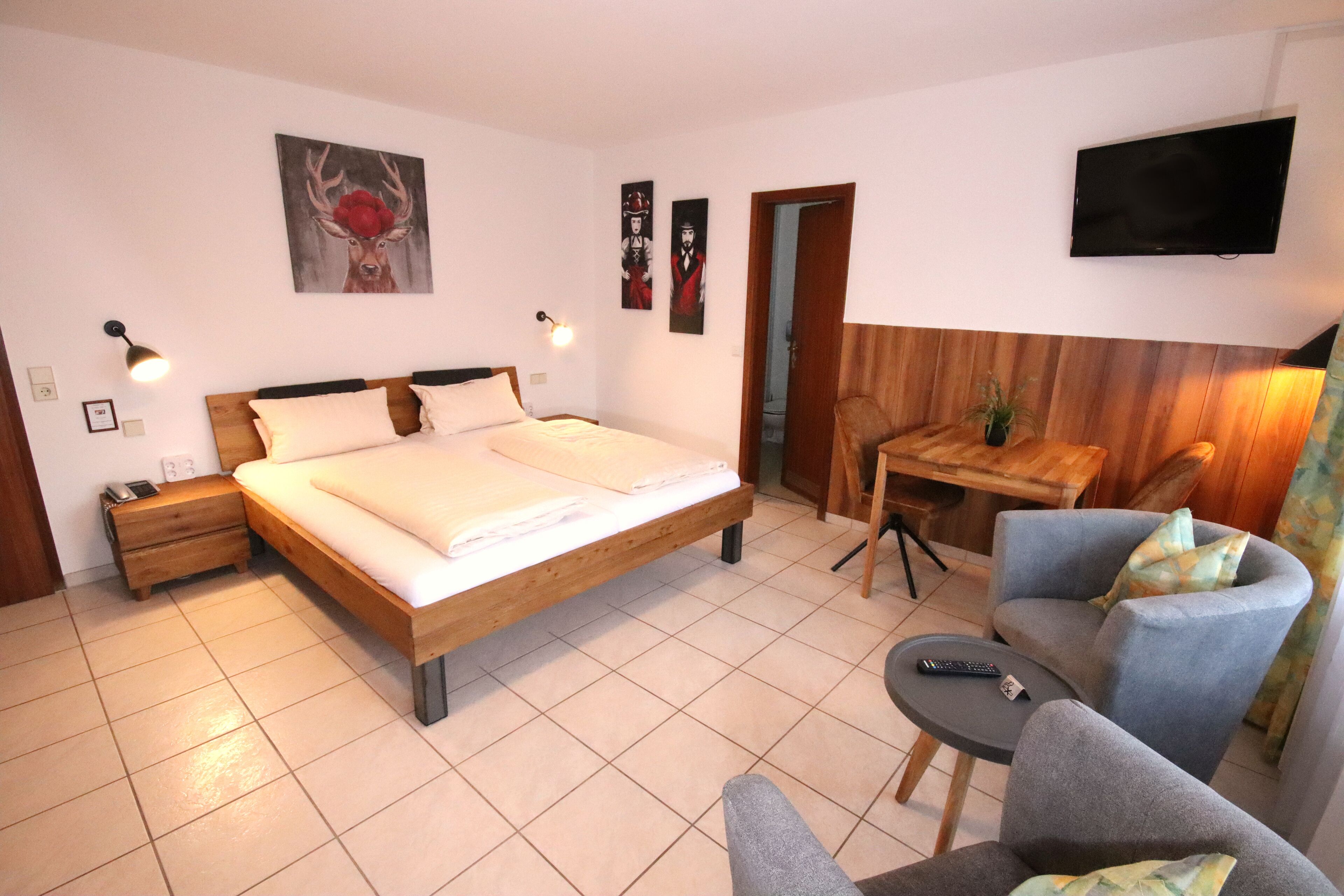 A bedroom with a bed, bedside tables, a desk, a chair, and a television.