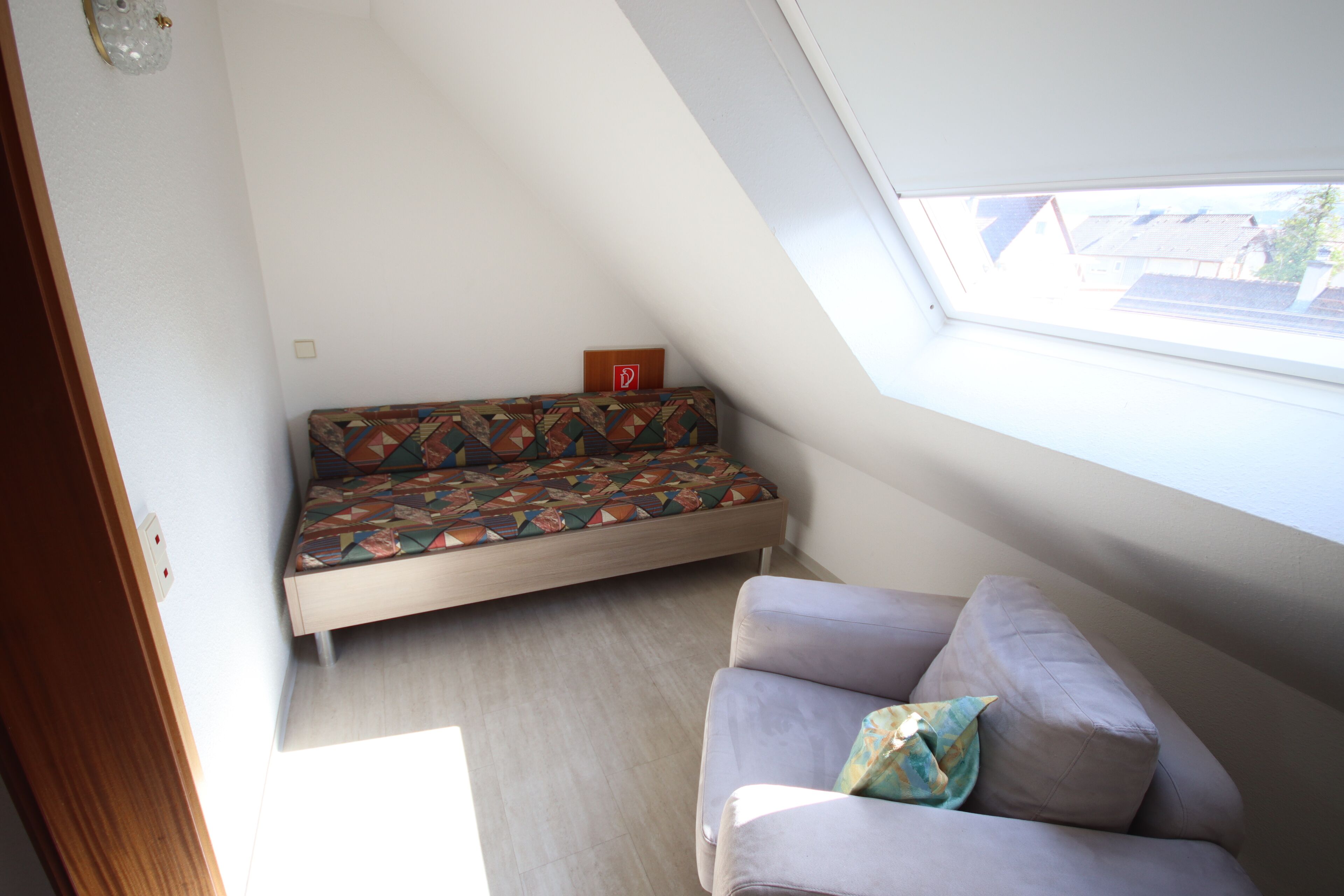 A room with a sloped ceiling, a sofa with a geometric patterned cushion, and a plain couch with a single pillow.