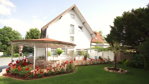 A house with a covered patio, a lawn, and red flowers. - Appartements Biedermeier (Bad Krozingen)