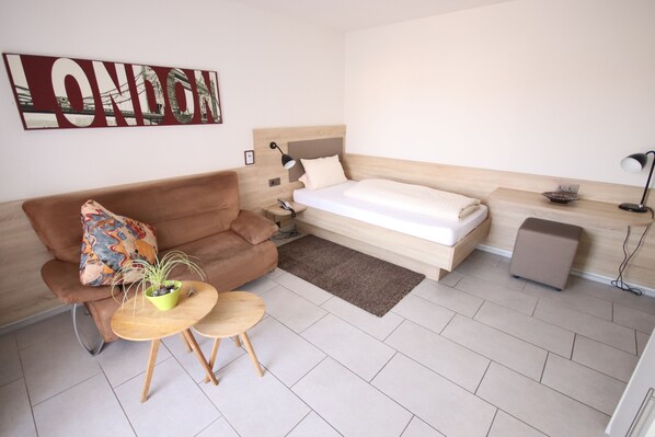 A modern bedroom with a bed, a sofa, a small table with a plant, and a wall-mounted artwork.