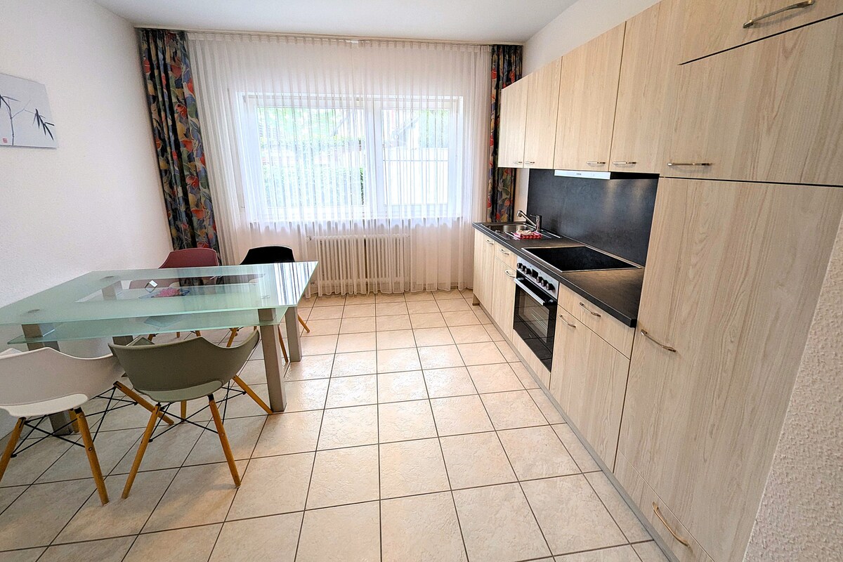 A compact kitchen with a glass dining table, wooden cabinets, and a built-in oven.