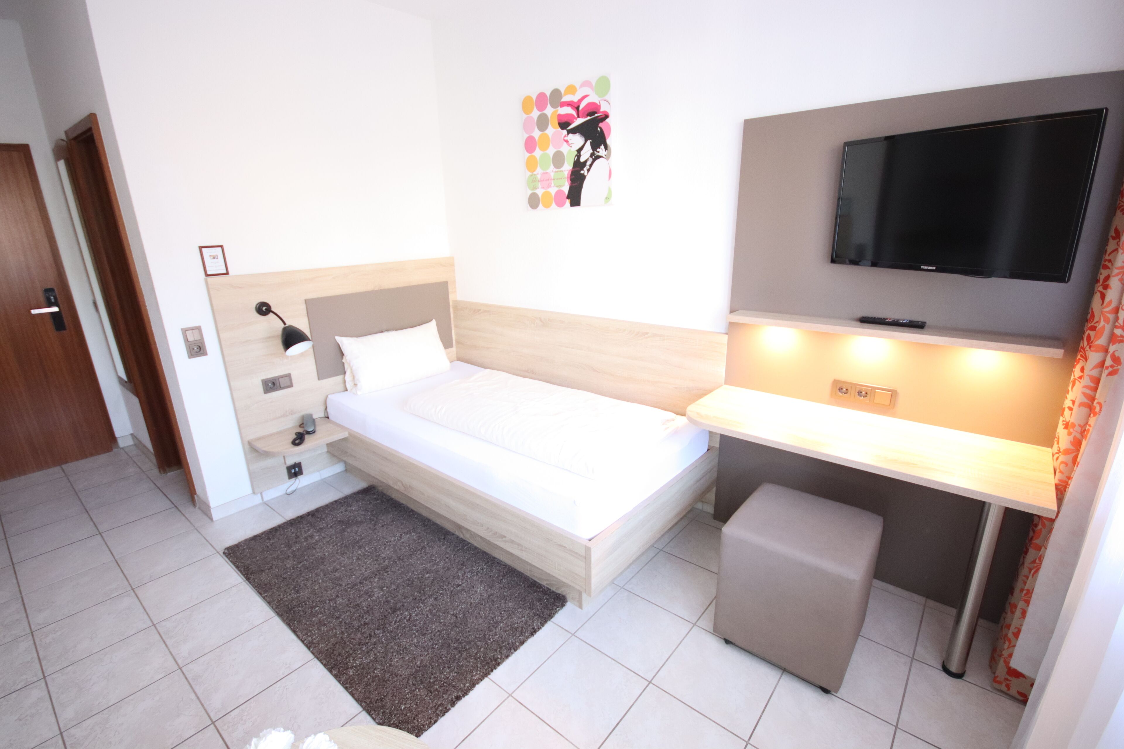 Una habitación de hotel con cama, escritorio, televisor y un taburete pequeño.