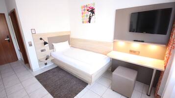 Una habitación de hotel con cama, escritorio, televisor y un taburete pequeño.