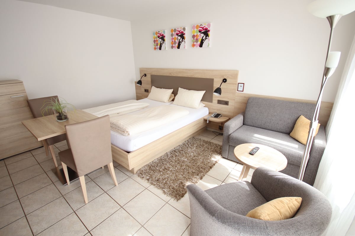 Un dormitorio moderno con una cama, mesitas de noche, un escritorio, una silla, un sofá y una lámpara.