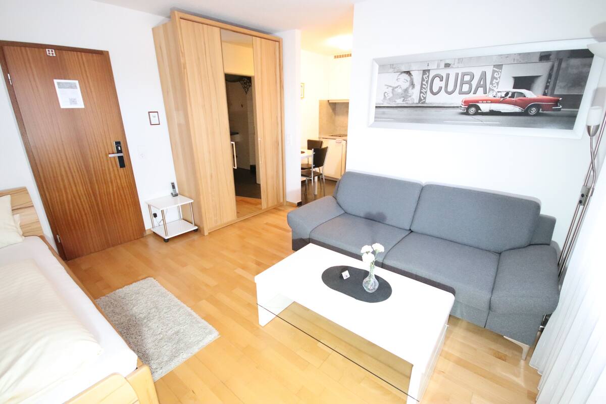 Un espacio habitable pequeño con un sofá gris, una mesita de centro blanca y una puerta de madera.