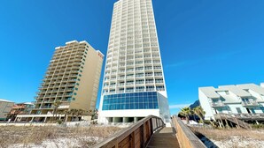 Um hotel moderno com fachada curva, várias varandas e um calçadão de madeira que leva à entrada.