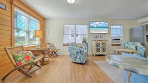 A living room with wooden floors, wicker furniture, a patterned sofa, a television, and a cabinet.