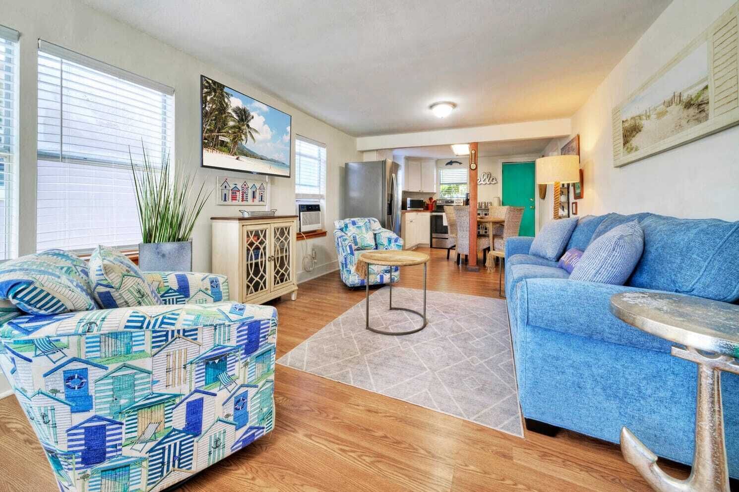 Un salon spacieux avec un canapé bleu, des fauteuils à motifs et un coin repas agrémenté d’une porte verte.