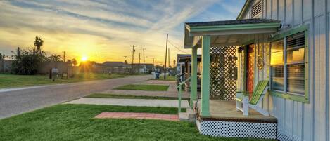 A single-story building with a porch, a small deck, and a view of the sunset.