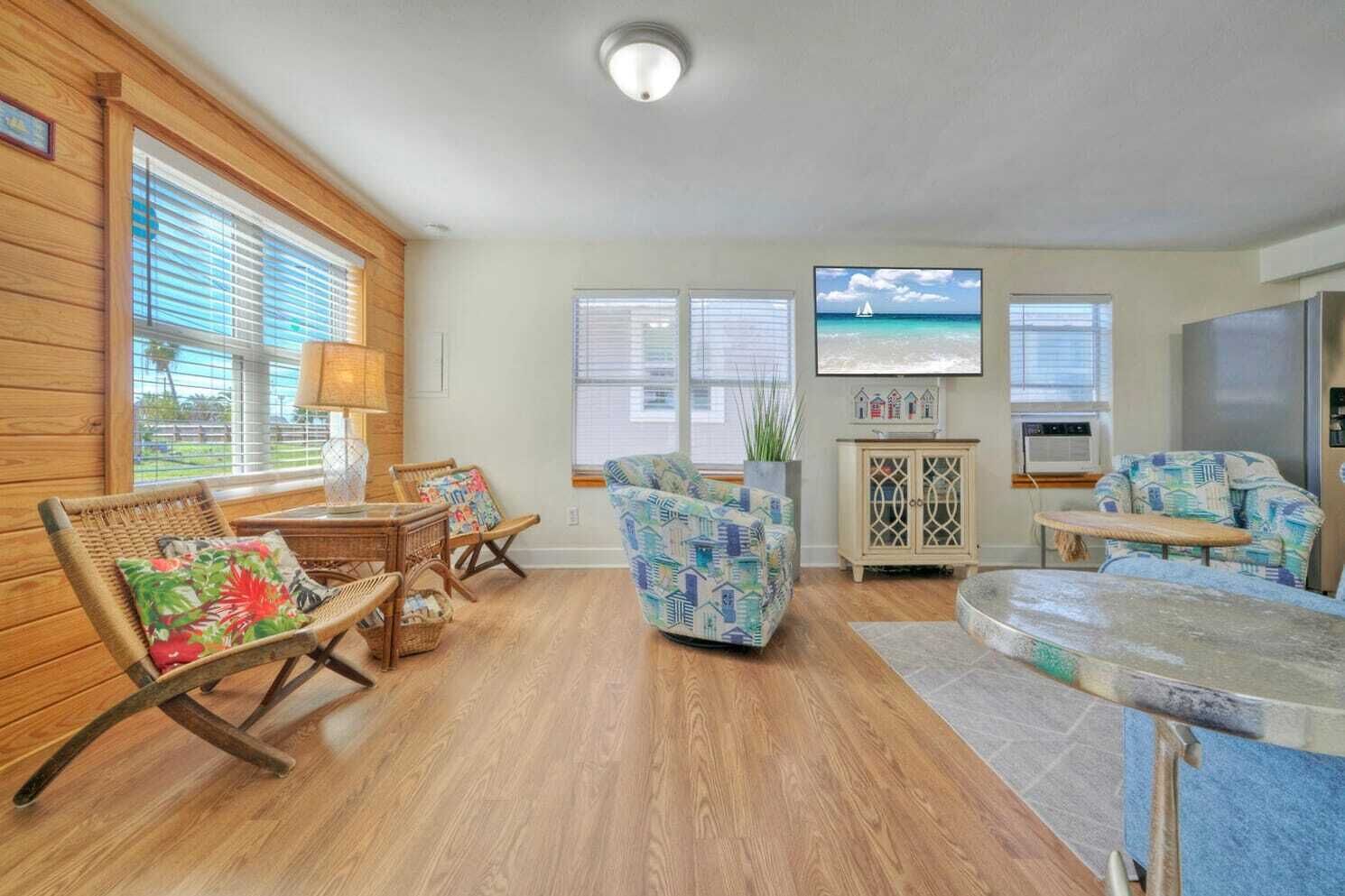 A living room with wooden floors, wicker furniture, a patterned sofa, and a television displaying a beach scene.