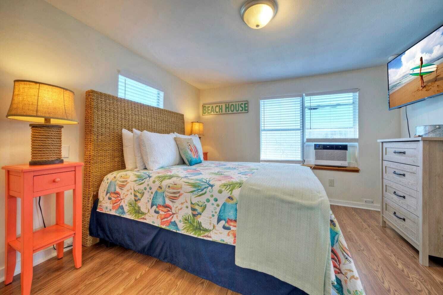 Un dormitorio con una cama, una mesita de noche, un tocador y un cartel en la pared que dice "BEACH HOUSE".