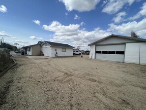 Une propriété située en zone rurale, avec une allée en terre battue, un petit bâtiment comprenant un garage, et un camion garé au fond.