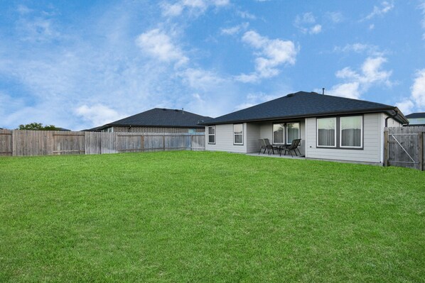 Une maison d’habitation avec une pelouse bien entretenue, une terrasse dotée de mobilier d’extérieur et une clôture en bois.