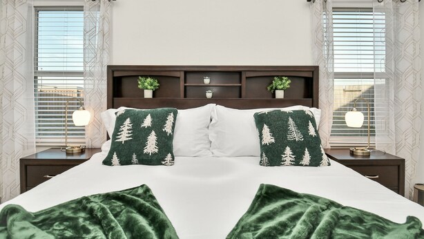 A neatly made bed with two pillows, a bedside table with a lamp, and a small shelf with plants. - Exquisite 3 bedroom house located in a very quiet area of Katy . (Katy)
