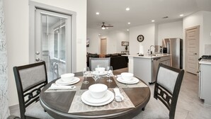 A dining area with a round table set for four, a kitchen in the background, and a living area with a couch and a TV. - Exquisite 3 bedroom house located in a very quiet area of Katy . (Katy)