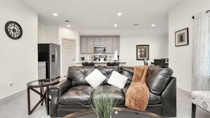 A modern living room with a leather sofa, a coffee table, and a kitchen in the background. - Exquisite 3 bedroom house located in a very quiet area of Katy . (Katy)