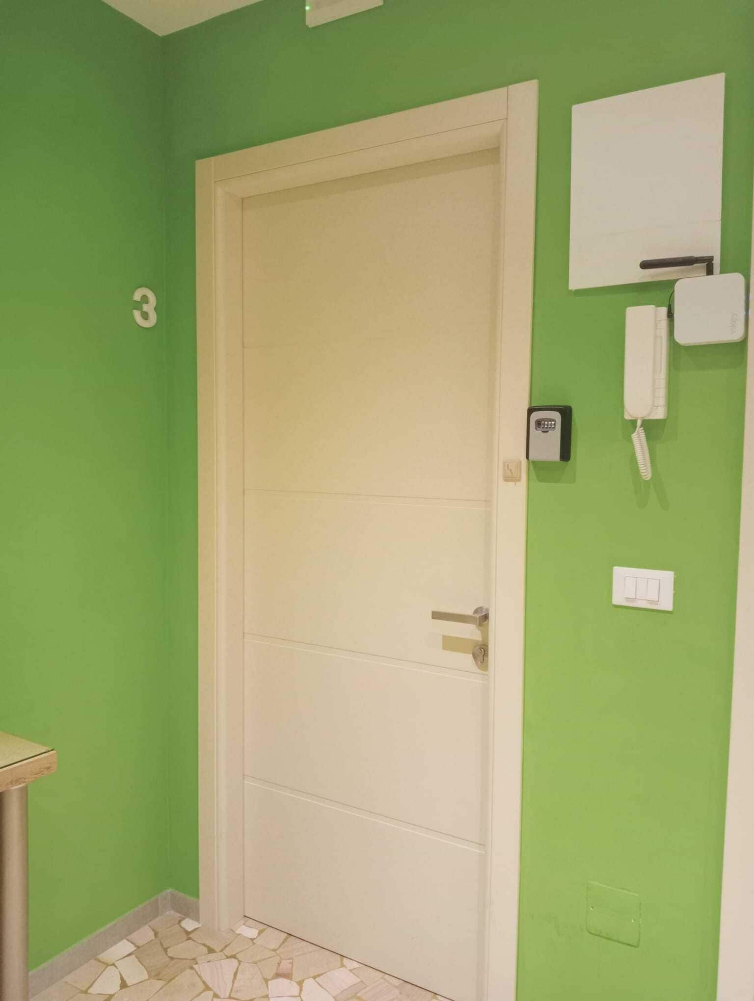 Une pièce avec un mur vert, une porte blanche, un petit bureau et un téléphone fixé au mur.