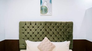 Ein Bett mit einem gesteppten Kopfteil, einem Kissen und einem an der Wand hängenden abstrakten Gemälde.