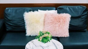 Eine schwarze Ledersofa mit drei flauschigen Kissen in Weiß, Beige und Rosa. Vor dem Sofa steht ein runder Marmor-Tisch mit goldener Basis.