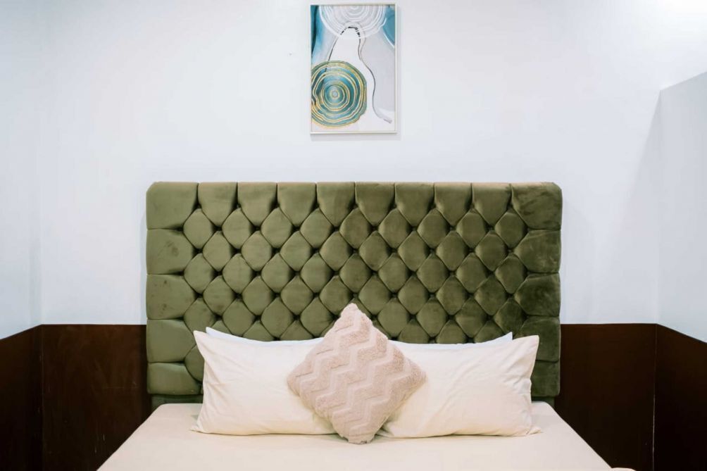 Una cama con cabecera capitonada, un almohadón y una obra de arte colgada en la pared.