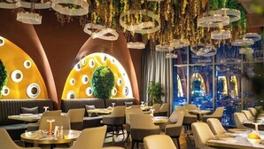 Restaurante com mesas redondas, assentos acolchoados e luminárias pendentes.