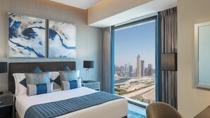 Quarto de hotel moderno com uma cama grande, uma mesa de trabalho e vista para a paisagem urbana.