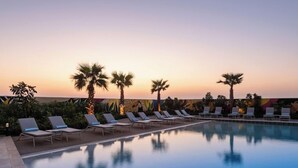 Área de piscina com espreguiçadeiras e palmeiras ao pôr do sol.