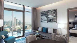Quarto de hotel moderno com uma janela grande que oferece vista para a cidade, um sofá, uma mesa de jantar e uma área de quarto separada.