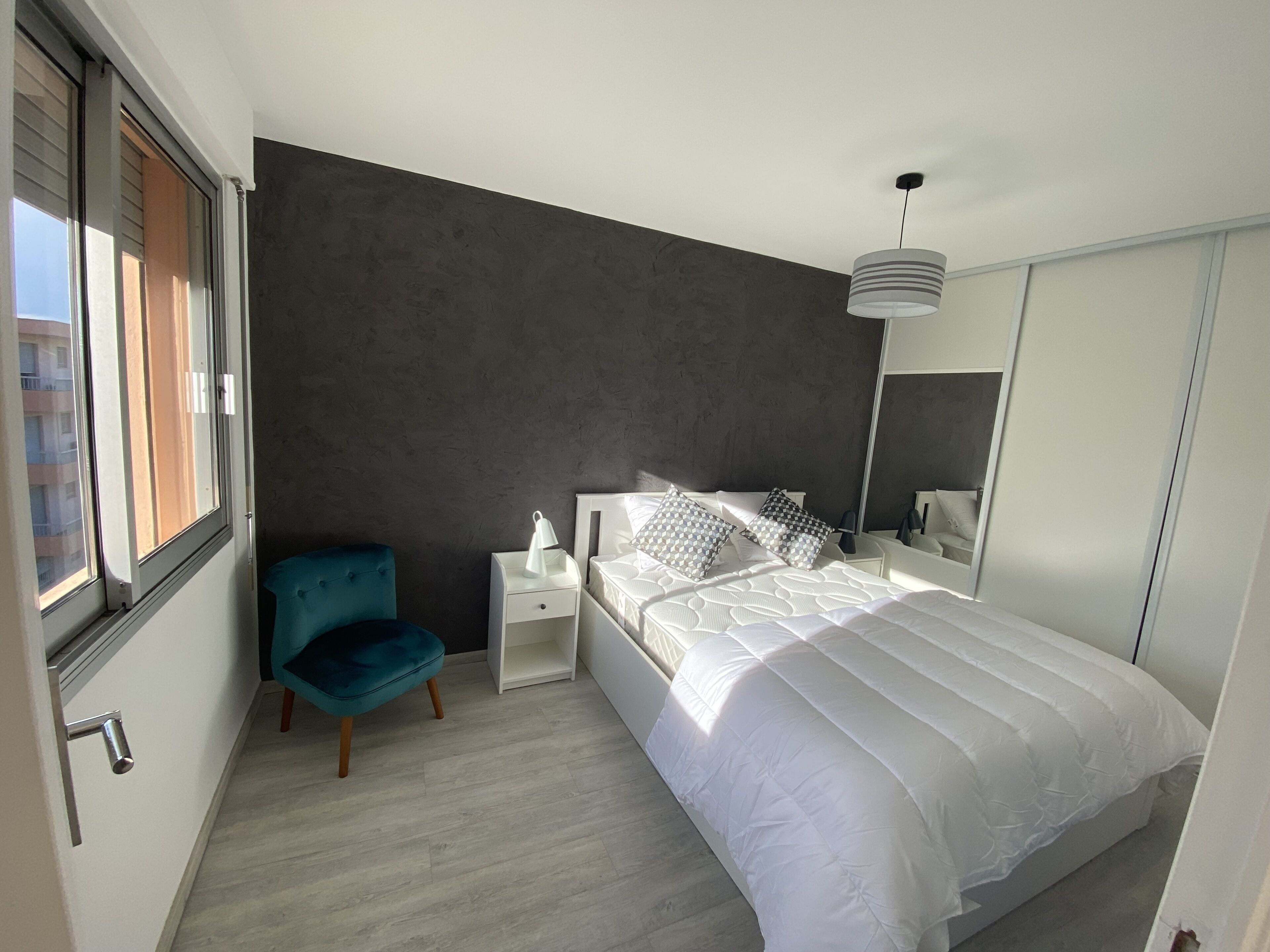 Een moderne slaapkamer met een groot bed, een nachtkastje, een blauwe stoel, een bedlamp en een kledingkast.