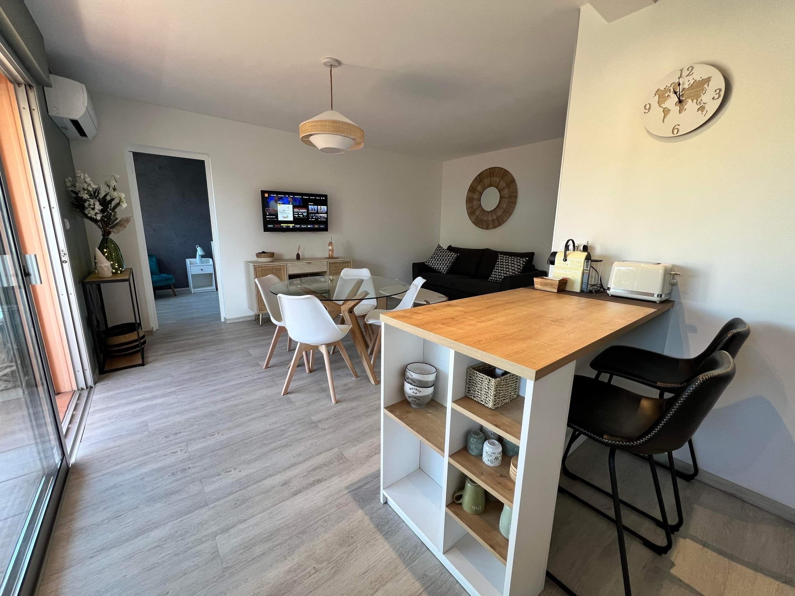 A modern kitchen with a wooden island, white chairs, and a TV mounted on the wall.