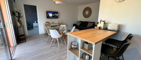 A modern kitchen with a wooden island, white chairs, and a TV mounted on the wall.