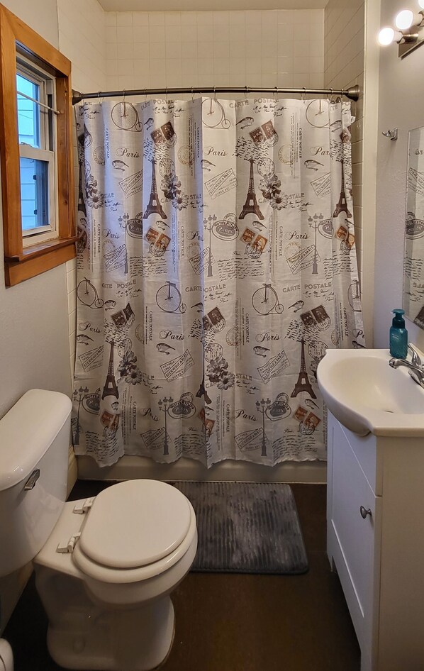 A bathroom with a shower curtain featuring Parisian motifs, a toilet, a sink, and a window.