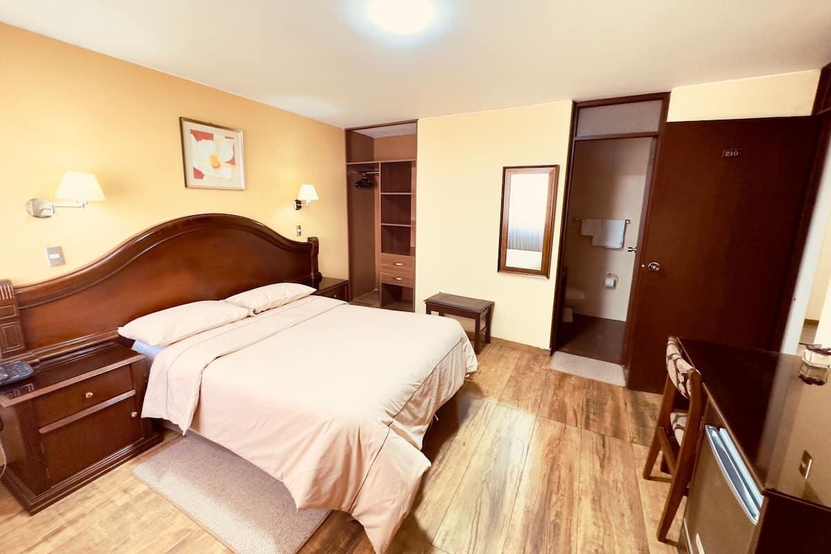 A hotel room with a wooden bed, bedside tables, a wardrobe, and a mirror.