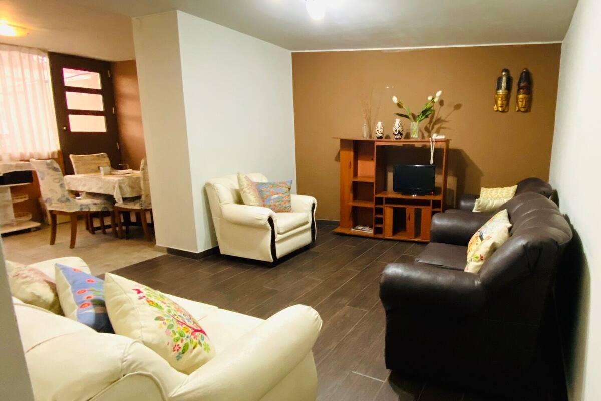 A living room with a sofa, armchairs, a TV stand, and a dining area with a table and chairs.
