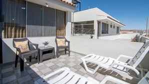 Una terraza en la azotea con mobiliario exterior, incluyendo sillas de mimbre y sillones blancos, junto a una pequeña mesa con un jarrón de flores.