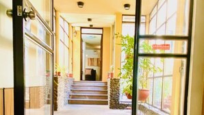 Entrada de un hotel con suelo de baldosas, una escalera que conduce al piso superior y plantas en macetas a lo largo de las paredes.