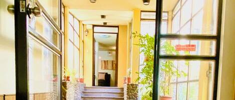 Entrada de hotel com porta de vidro, escada que leva ao andar superior e plantas em vasos ao longo do caminho.