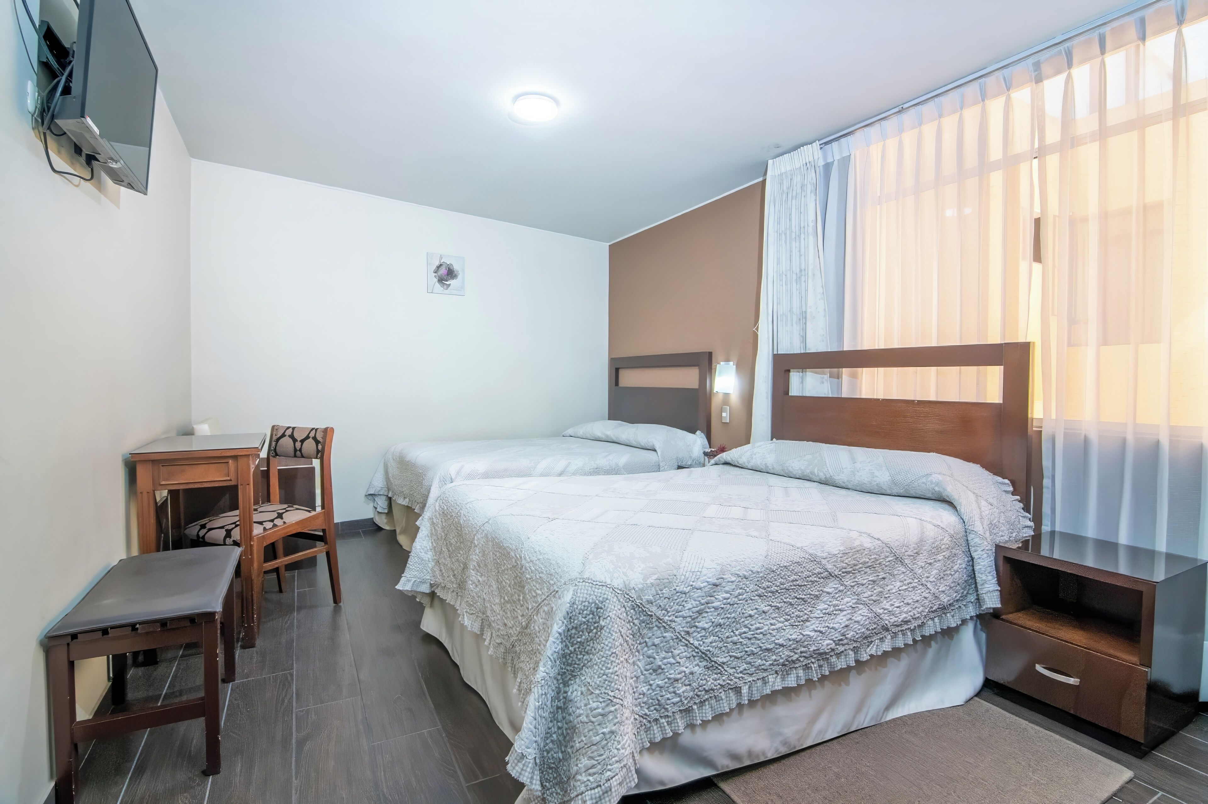 A hotel room with two beds, a desk, a chair, a TV, and a window with curtains.