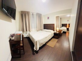 Habitación de hotel con cama, escritorio con silla, televisor montado en la pared y una pequeña mesa con una planta.