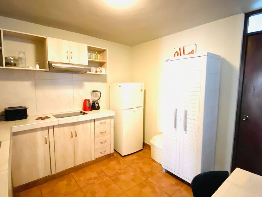 Una cocina compacta con alacenas blancas, un refrigerador, un lavamanos y una cafetera.