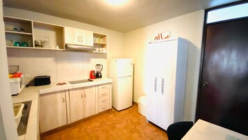 A compact kitchen with white cabinets, a refrigerator, a sink, and a coffee maker.
