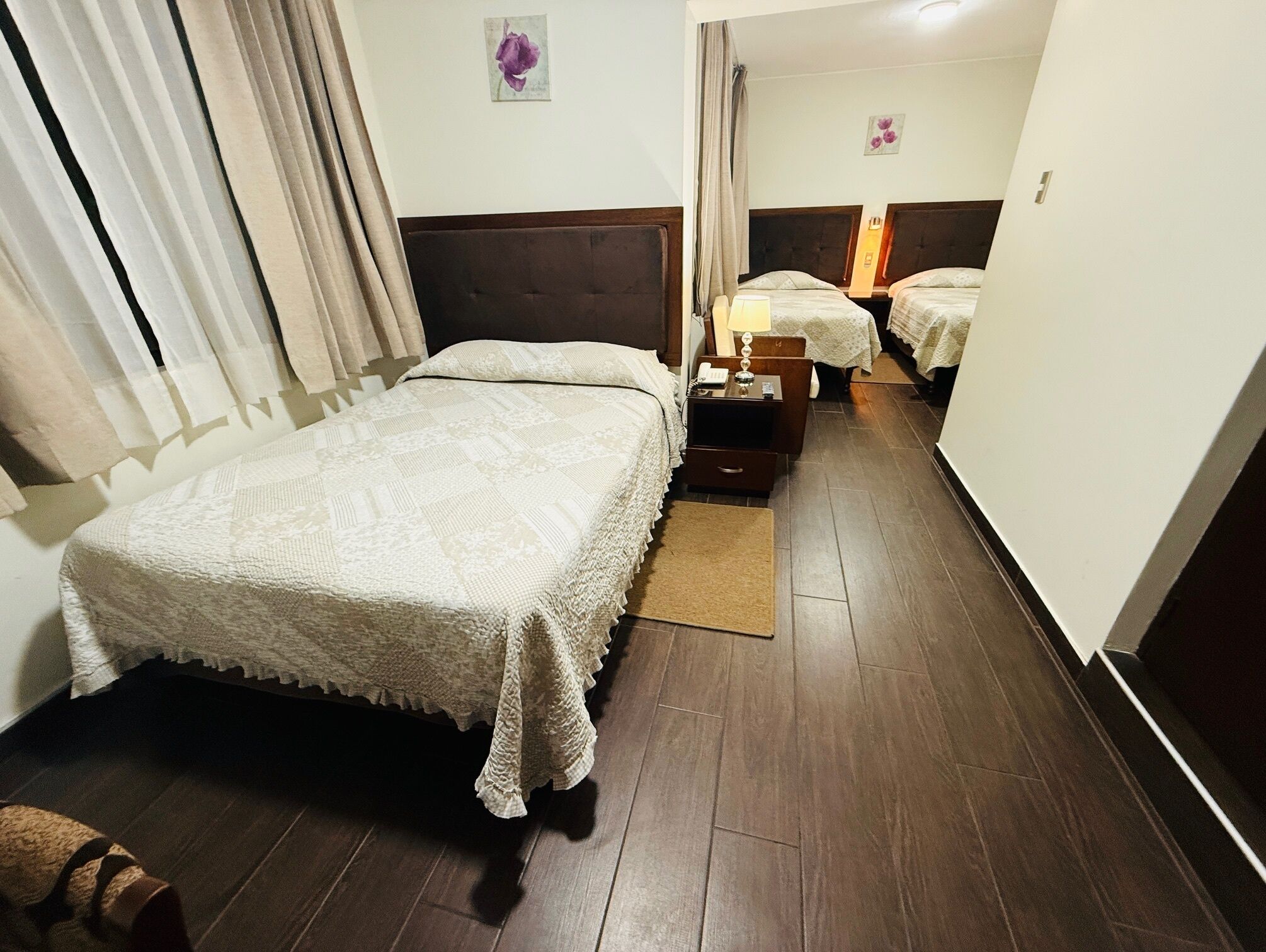 Une chambre d’hôtel avec un grand lit, un lit plus petit, une table de chevet avec une lampe et un plancher en bois.
