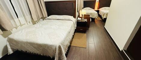 Une chambre d’hôtel avec un grand lit, un lit plus petit, une table de chevet avec une lampe et un plancher en bois.