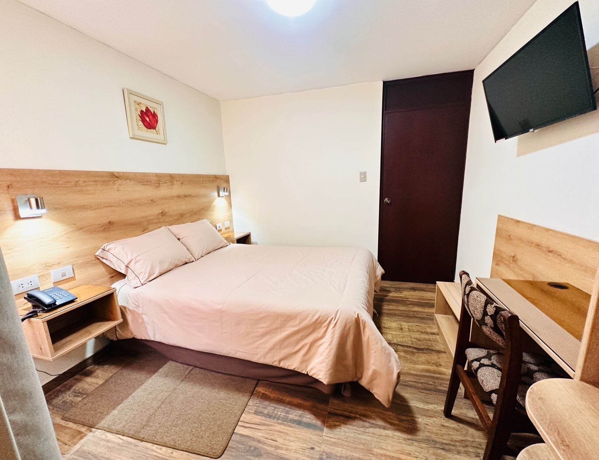 Une chambre bien rangée, avec un lit, une table de chevet, une lampe et un téléviseur fixé au mur.