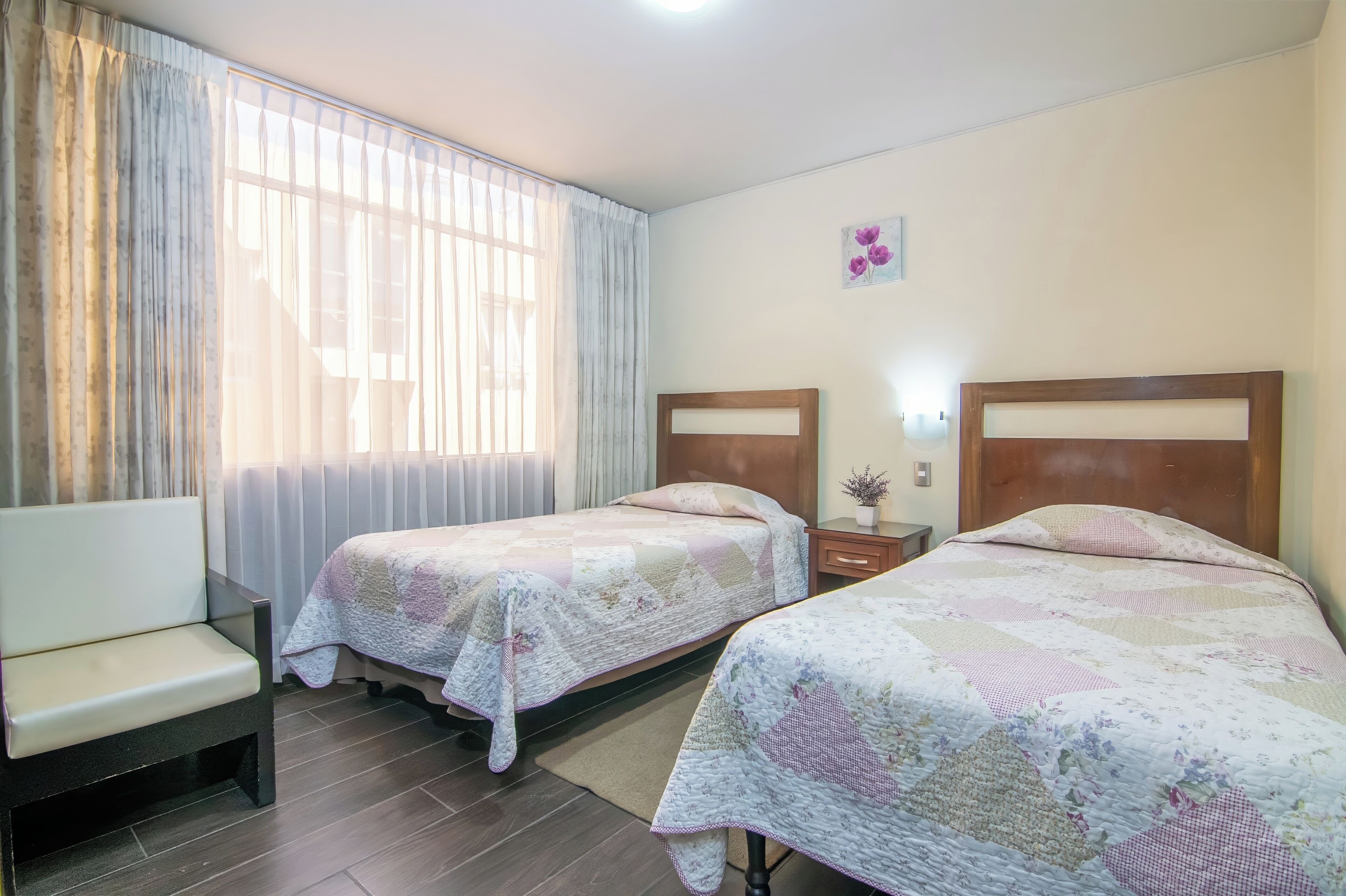 A hotel room with two beds, a sofa, a window with curtains, and a small wall decoration.